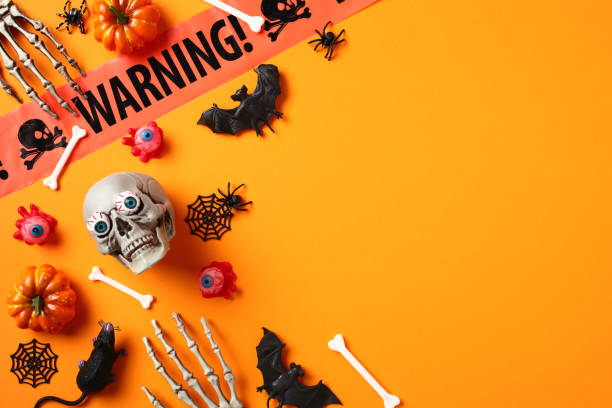 istock Happy Halloween flat lay composition. Skull with bloody eyes, pumpkins, bats, spiders, warning tape on orange background 1584428896