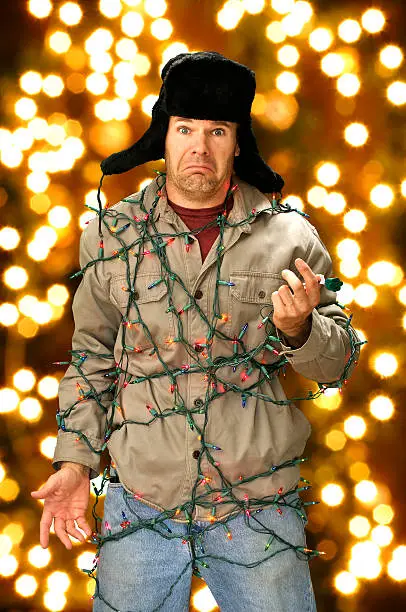 Funny confused man wrapped in colorful Christmas lights