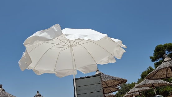 Low angle view of an opened beach fabric umbrella against the blue sunny sky, view from under parasol, holiday or vacation concept, with copy space