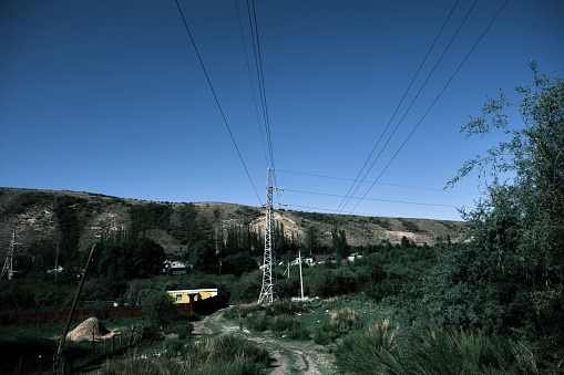 Outdoor grill on grass covered ground with homes sky and mountain background. Electricity towers and cable wires can also be seen in this landscape.