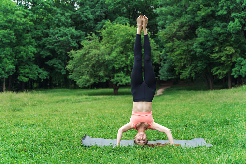 Headstand. Girl doing yoga in a clearing in the park and stands on her head.