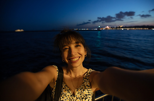 Young woman is taking a selfie with Istanbul cityscape on ferry at after sunset.