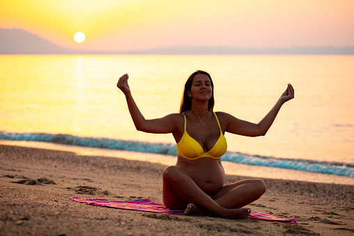 Photo of a pregnant woman doing yoga at the seaside in sunrise