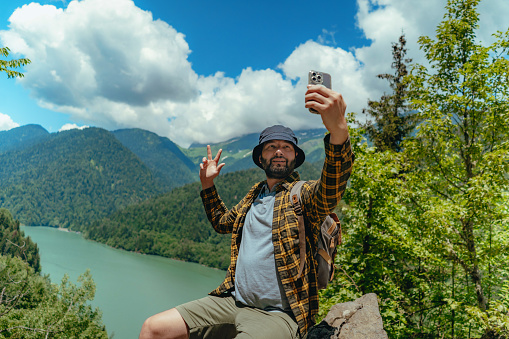 Hiking traveller handsome caucasian bearded man with backpack taking selfie against view of Lake Ritsa in Abkhazia