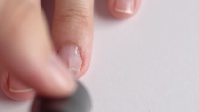 Selfmade manicure service. Manicurist paints nails with transparent polish, macro. Nail polish application. Manicured nails.