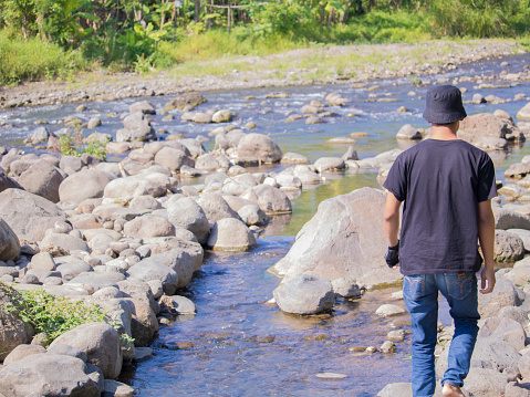 Young man crossing the stream. Jumping on rocks