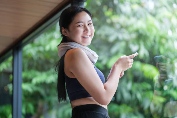 istock Smiling young sportswoman using smartphone at gym while relaxing after training. 1584595299