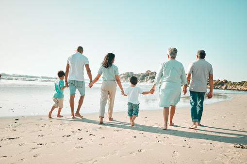 Big family, holding hands and walking outdoor on beach with children, grandparents and parents . Men, women and boy kids walk by sea for summer travel vacation or holiday with love, care and support