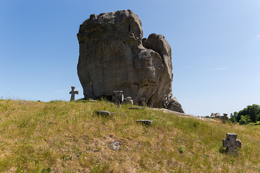 Single sandstone rock, as remains of the ancient sea reef, on the hill with stone crosses of medieval Cossack graves on a foreground against the clear sky. Pidkamin village, Ukraine