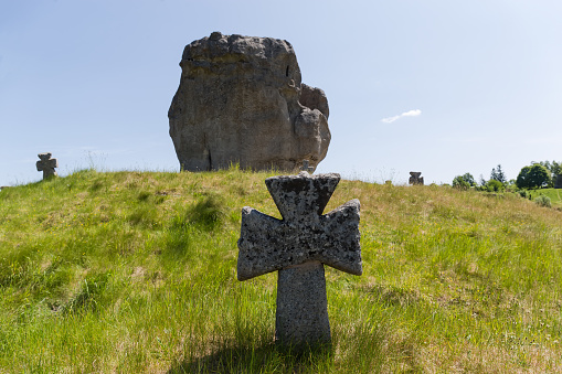 Old stone cross on the medieval Cossack grave on the hill overgrown with grass against the big single sandstone rock. Pidkamin village, Ukraine