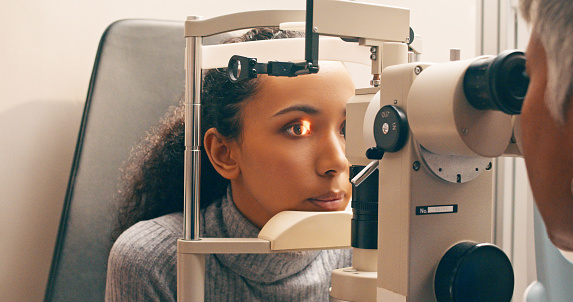 Optician, test and eye exam or care of a woman or customer for vision, eyesight and lens. Optometrist and person at machine or light for healthcare consultation for optometry or ophthalmology service