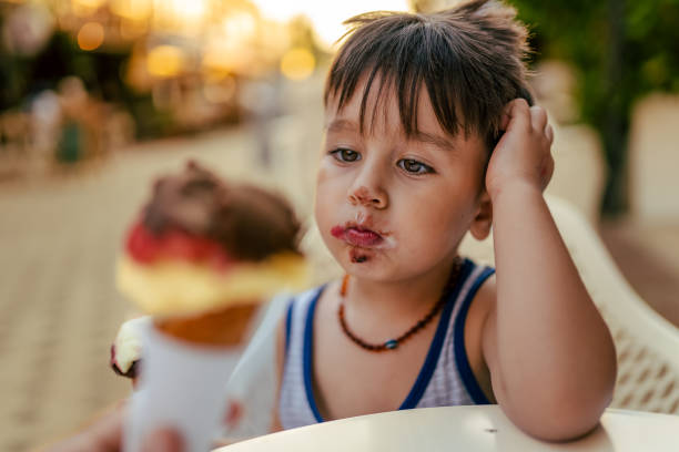 netter kleiner junge genießt es, im sommer eis zu essen - child chocolate ice cream human mouth stock-fotos und bilder