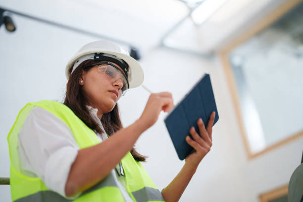 istock Woman wearing protective white helmet, using digital tablet at the construction site 1584652159