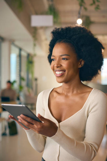 istock Businesswoman Standing In Busy Office Using Digital Tablet 1584652699