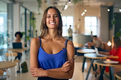 Portrait Of Smiling Young Businesswoman Standing In Busy Office