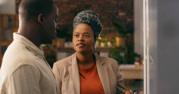 istock Business people, teamwork and planning on glass board for night solution, brainstorming or problem solving ideas. Time management, project collaboration and professional african woman and man goals 1584665341