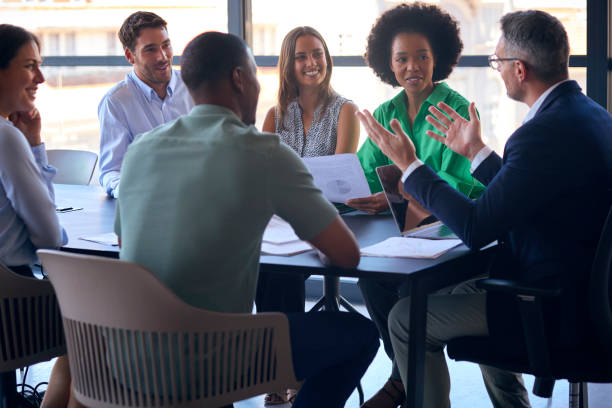istock Multi-Cultural Business Team Meeting Around Office Boardroom Table With Laptops Discussing Documents 1584668124