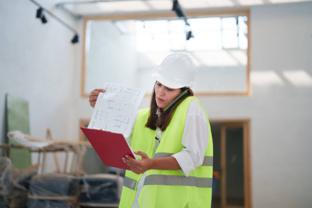 istock Woman wearing protective white helmet, with blueprints at the construction site 1584668660