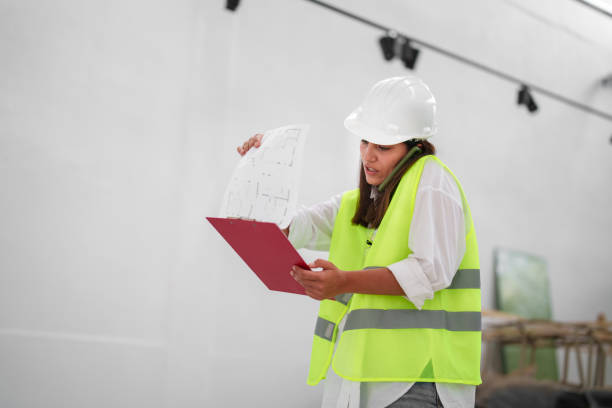 istock Woman wearing protective white helmet, with blueprints at the construction site 1584671118