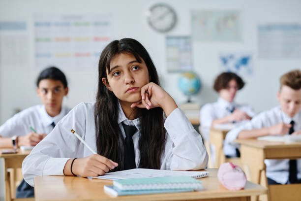 Schoolgirl sitting at her desk and listening to teacher during lesson