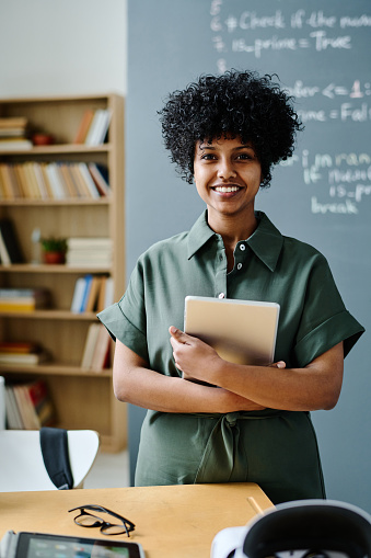 Portrait of young African American IT teacher with tablet pc smiling at camera while standing in class