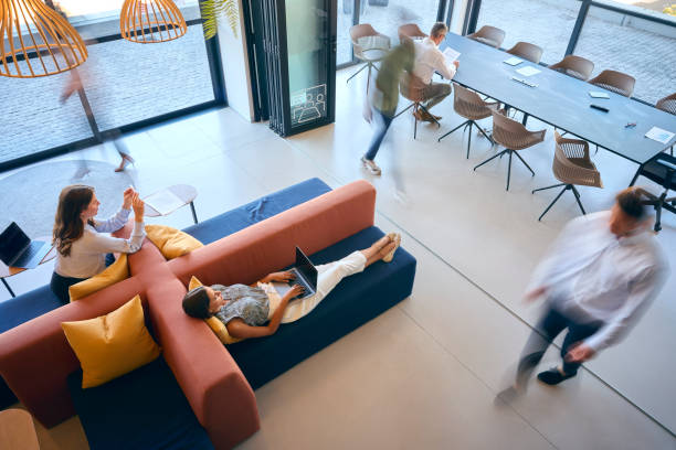 istock Overhead View Of Modern Open Plan Office With Staff Working Around Table And Breakout Seating Area 1584683811