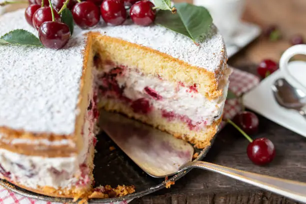 Traditional german cherry cream cake. Served whole and ready to eat with cross section view on rustic and wooden table background. Front view, closeup