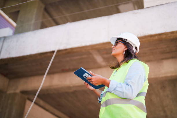 istock Woman wearing protective white helmet, using digital tablet at the construction site 1584684227
