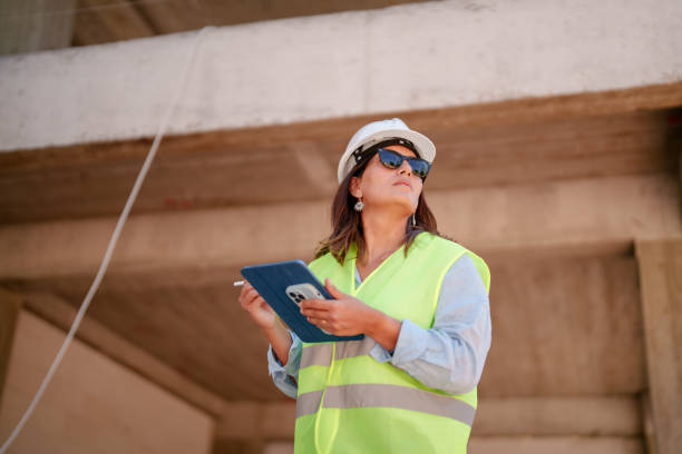istock Woman wearing protective white helmet, using digital tablet at the construction site 1584684228