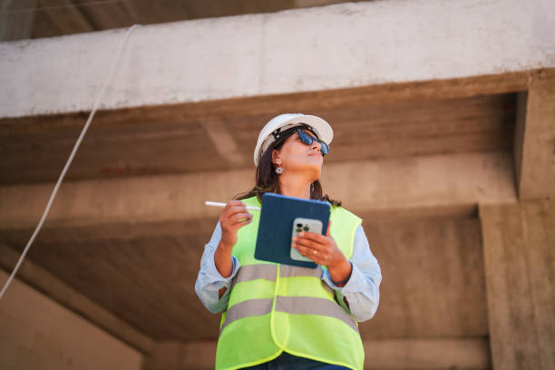 istock Woman wearing protective white helmet, using digital tablet at the construction site 1584684391