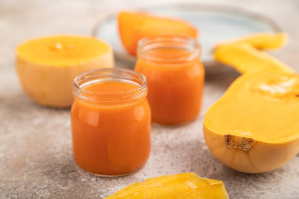 istock Baby puree with pumpkin, persimmon, mango in glass jar on brown concrete, side view, selective focus 1584688934