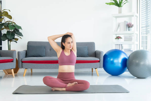 Asiatische junge gesunde Frau in Sportartikeln, die Yoga zu Hause praktiziert, Sportmädchen, das im Wohnzimmer zu Hause meditiert – Foto