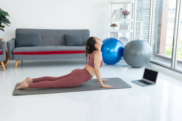 Asiatische junge gesunde Frau in Sportartikeln, die Yoga zu Hause praktiziert, Sportmädchen, das im Wohnzimmer zu Hause meditiert – Foto