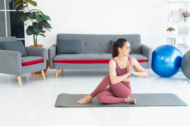 Asiatische junge gesunde Frau in Sportartikeln, die Yoga zu Hause praktiziert, Sportmädchen, das im Wohnzimmer zu Hause meditiert – Foto