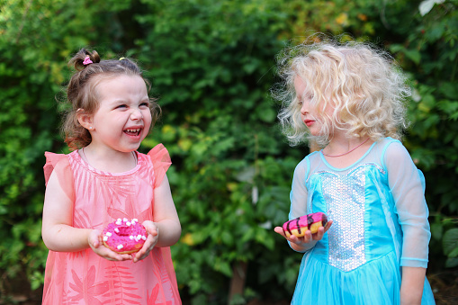 Cute little girls laughing and holds pink donuts