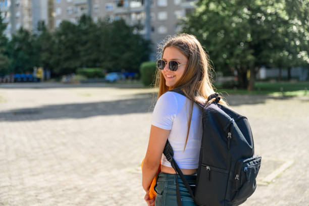 Teenage girl with black backpack and sunglasses wearing modern casual clothes looking over her shoulder in a residential district.