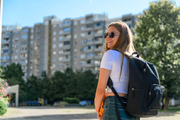Teenage girl with black backpack and sunglasses wearing modern casual clothes looking over her shoulder in a residential district.