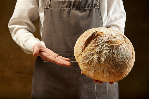 Baker holds freshly baked homemade sourdough bread. Concept of food, health, traditions, bakery and ad