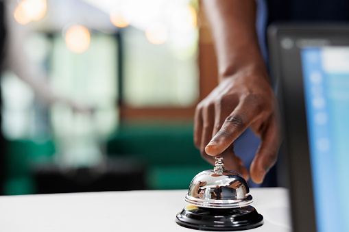 Detailed image of male client ringing service bell at front desk requesting assistance with check-in process at tropical hotel. Tourist using urgency bell to call for employee at reception.