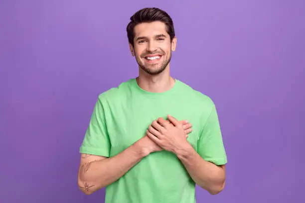 Photo of Photo of young smile guy hands touch chest heart thankful grateful appreciate you for support his team isolated on purple color background