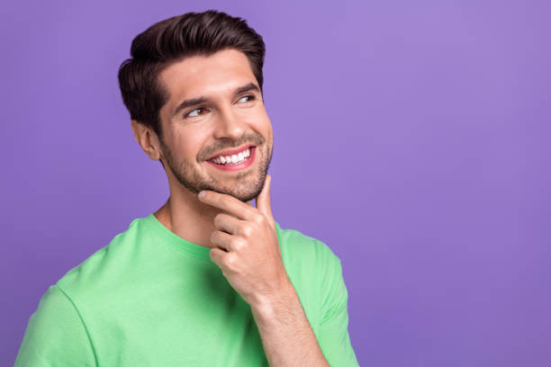 Portrait photo of young thoughtful guy touch chin looking empty space minded virile unshaved bristle isolated on violet color background stock photo
