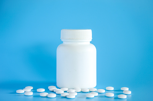 White plastic pill bottle with teblets pills on blue background with selective focus