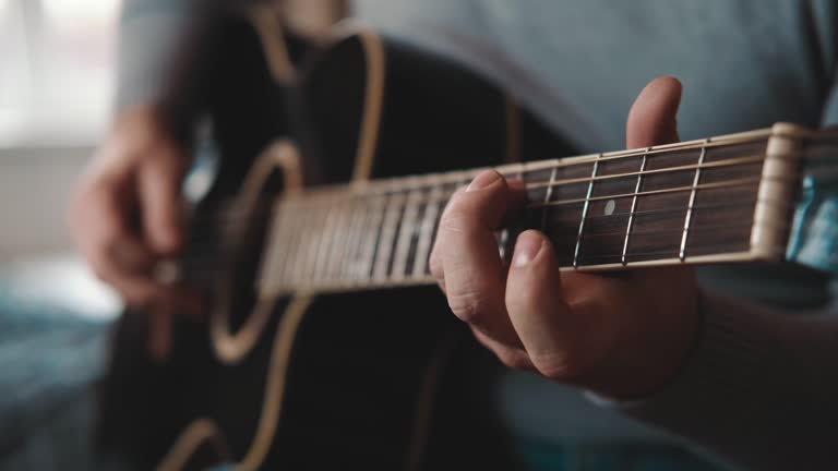 Playing the guitar. Strumming acoustic guitar. Musician plays music. Man fingers holding mediator. Man hand playing guitar neck in dark room. Unrecognizable person rehearsing, fretboard close-up.