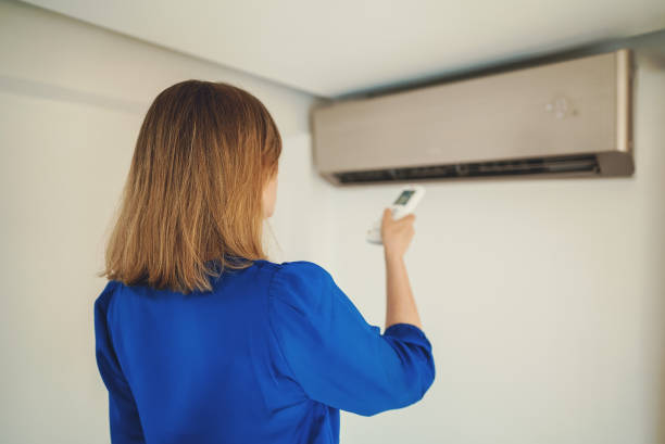 istock Woman holding remote control aimed at the air conditioner. 1584849119