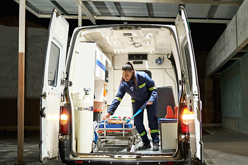 Full length view of uniformed woman standing in emergency vehicle and straightening spinal board on portable stretcher.