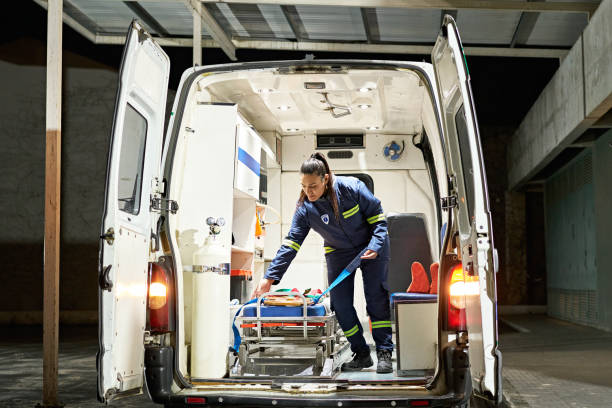 Young female paramedic organizing ambulance interior Full length view of uniformed woman standing in emergency vehicle and straightening spinal board on portable stretcher. medic stock pictures, royalty-free photos & images