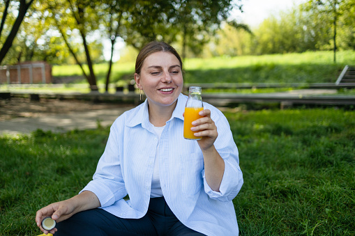 Female hand takes healthy smoothies drink in summer, having breakfast, drinking orange juice outdoors at city park