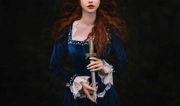 istock Fantasy woman warrior on black background, lady with red lips hands close up holding dagger, knife short sword. Girl gothic princess witch. Vintage blue dress old style. Art photo cropped face. ancient costume, hair fly in wind motion 1584862745