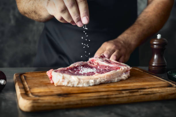 istock Man cook sprinkles salt on raw beef steak on the bone 1584865447