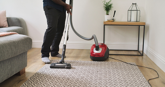 Cleaning, carpet and a person with a vacuum cleaner in a home lounge for dust, dirt and maintenance. Legs of an adult with an electric appliance for vacuuming living room floor in a clean house